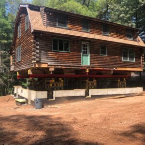 A cabin-style house lifted above the ground, supported by steel and lifting beams - Payne Construction Services