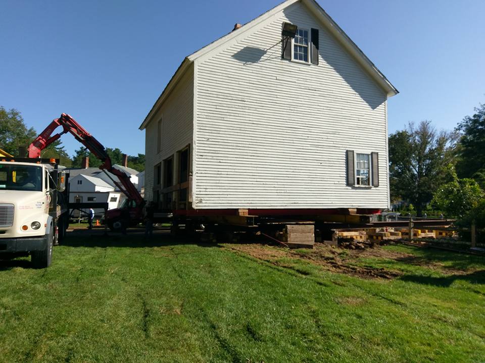 An old colonial house is loaded onto the bed of a truck.