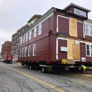 A house with boarded up entrances is carted down a street.