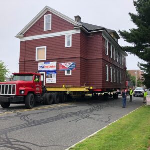 A red house is carefully carted through a town.