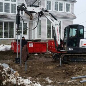 Team of contractors screwing in a helical pile in front of a house - Payne Construction Services