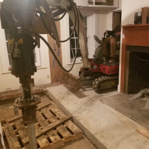 A home's interior floor dug out and helical piles being installed - Payne Construction Services