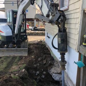 Construction machinery screwing in helical pile near foundation - Payne Construction Services