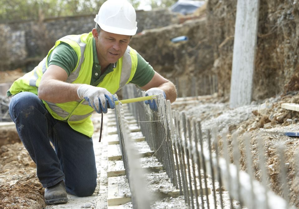 a man in safety gear measuring a row of metal bars